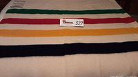 Full view of white wool blanket with horizontal stripes in green, red, yellow and navy