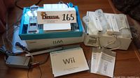 Full view of Nintendo Wii console in box with manuals and power adapter. Shows console, sensor bar, power supply, manuals, and box.
