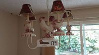 Front view of chandelier hanging from ceiling showing five arms with rooster figurines and shades