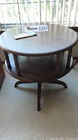 Full view of the round wooden drum table showing the circular top and lower shelf with turned vertical supports