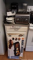 Countertop with stainless steel four slice KitchenAid toaster, white Chef's Choice sharpener, Hamilton Beach small grill, and boxed Black & Decker family size griddle.