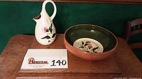 Photo of 10 inch cream-colored Stangl Pottery pitcher with thistle floral design and 12 inch round bowl with terracotta rim and dark green interior with matching floral design.