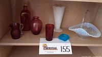 Shelf display of seven vintage glass items including cranberry red, blue, and milk hobnail glass pieces