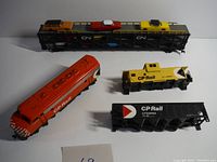 Four model rail cars including two locomotives and two rail cars carrying model cars, arranged on a flat surface.