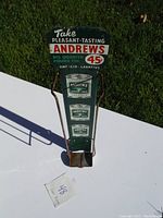 Full view of the vintage metal display sign standing upright on white surface, showing overall condition and size against grass background.