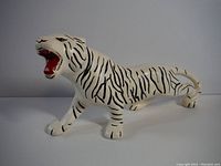 Front right side view of ceramic white tiger figurine showing painted black stripes and red inside mouth.