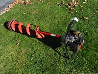 Full view of the red Eskimo gas powered ice auger laid on grass showing the spiral drill bit and engine with black handle grips.