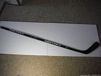 Full view of the black hockey stick lying horizontally on white surface for condition assessment and overall view