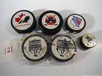 Group of seven hockey pucks featuring Team Canada, New York Rangers, USA Park City, International Hockey Championship Under 17 Kitchener (two signed and sealed), and a small NHL shark logo puck.