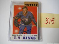 1970 Eddie Shack autographed hockey card in clear plastic toploader showing tape residue on holder, card in good condition.