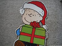 Front view of vintage Charlie Brown cardboard cutout holding present wearing Santa hat