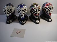 Front view of four miniature goalie masks featuring Patrick Roy, Ken Dryden, Rod Gilbert, and Jocelyn Thibeault, mounted on stands with player names and logos.