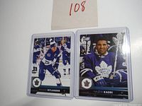 Photo of William Nylander and Nazem Kadri hockey cards in plastic holders, showing full front images of players in Toronto Maple Leafs uniforms.