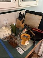 Wide view of cast iron pans, cutting boards, knife block, salt and pepper shakers, glass, ceramic spoon rest, and cookie jar.