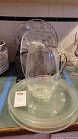 Set of five cut glass serving platters arranged standing behind a clear glass pitcher placed on top of a large microwave tray, showing overall condition and decorative patterns on the platters.
