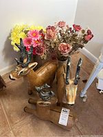 Group of three paper mache reindeer with varying sized black and white antlers, alongside multiple faux floral bunches in a corner, on tiled floor.