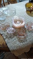 Overview of seven pink glass bowls, creamer, cup and saucer, and other pink glass items on table with patterned cloth.