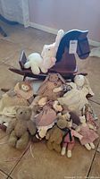 Vintage wooden rocking horse surrounded by various vintage stuffed bears and dolls arranged on the floor.