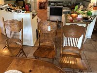 Front view of three solid pine carved dining chairs placed near a wooden table in a kitchen setting.
