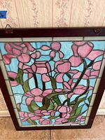 Close-up of stained glass panel with pink flowers and green leaves in a wood frame showing front detail.