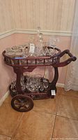 Front view of tea cart showing two shelves, spindle railing, and assorted glassware on shelves (not included in sale)