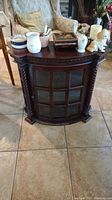 Full view of vintage mahogany curio cabinet with several decorative items arranged on top including music box, vases, and figurines.