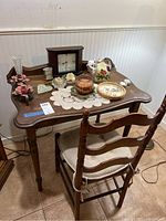 1930s wooden desk with various decorative items on top including clock, candle holder, small bowls, and plates on a crochet doily. Desk has curved edges and carved legs, drawer with keyhole visible.