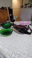 Photo showing vintage glassware items including purple glass swan, green candy dish, green bowls, pink and white swirl bowl, and cranberry wine glass on table.