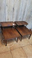 Pair of vintage walnut solid wood side tables shown side by side on a tile floor with wood panel background.