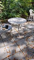 Front view of round wrought iron table set on stone patio with leaves scattered around