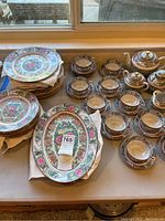 Overall group shot of vintage Asian porcelain china including plates, platters, cups, saucers, teapot, sugar bowl, and creamer. Items display colorful floral and Asian motifs with pink flowers and gold medallions.