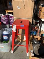 Single red metal bar stool placed outside the storage area showing protective white caps on legs.