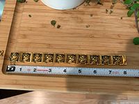 Full length view of the gold-tone Siam bracelet on a measuring tape, showing length close to 8 inches, placed on bamboo surface.