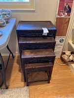 Four dark brown wooden carved nesting tables stacked, view front