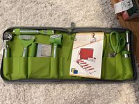 Zippered green fabric case open showing the garnishing tools including peelers, scissors, scoop, and zester alongside the Instant Counter food prep board pamphlet.