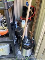 Full view of Grainfather brewing machine with digital controller, heat exchanger coil on top, and wooden broom leaning against brewing unit