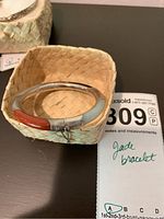 Front view of silver bangle bracelet with reddish-orange jade inlay inside woven basket