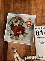 Photo of carved jade charm bracelet with various jade beads and charms, two round reddish pendants with gold dragon designs, a translucent jade charm, and part of a pearl necklace.