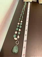 Full length necklace showing green faceted jade and white irregular pearls with silver tone loops next to a measuring tape showing about 13 inches long.