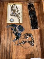 Overview of jewelry pieces including butterfly hair pin, circular pendant, stone and metal necklace, faceted bead necklace, and black hair pins in packaging.