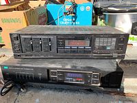 Two stacked audio units in outdoor setting with visible packaging boxes in background. Top unit Kenwood KR-4140 receiver, bottom unit Classique T-901 tuner. Surface dust and signs of use evident.