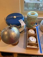 Photo showing meal carrier, globe, ice bucket, and ceramic bowls on a table near window.