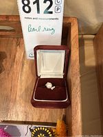 Pearl ring displayed inside a red velvet ring box with white satin lining, positioned on a wooden surface.