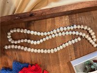 Pearl necklace and bracelet laid out on wooden surface with red and blue fabric tassels partially visible