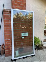 Full view of the large rectangular window standing outdoors, showing white frame and double-paned clear glass.