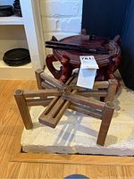 Dark reddish wooden tripod plant stand and light wooden folding plant stand and picture easel on floor near white brick wall.