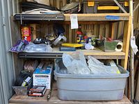 Wide view of metal shelves containing plumbing-related items: toolbox, drain cleaner, containers, WD-40 cans, hammer, and trowel.