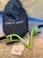 Embera Core Fit Hoop in lime green with black grips and black carrying bag with "Core Fit Hoop" label, instruction manual visible.