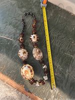 Full view of the shell necklace laid flat with a measuring tape alongside showing approximate length.