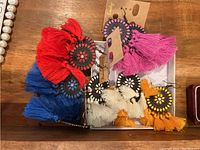 Top-down view of all five sets of tassel earrings in multiple colors arranged together on a wooden surface.